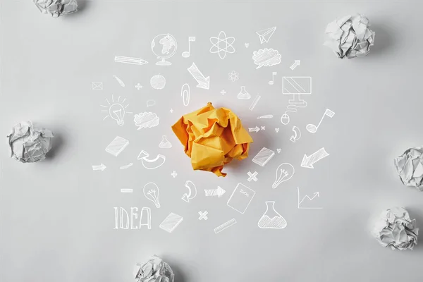 Vista dall'alto della carta gialla accartocciata circondata da icone di idee commerciali e carte bianche accartocciate sulla superficie bianca — Foto stock