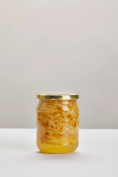 Vue rapprochée du bocal en verre avec du miel sur une surface blanche sur fond gris — Photo de stock