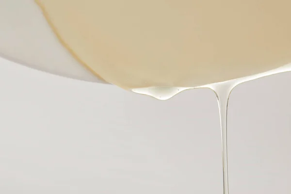 Close up view of honey flowing from white plate on grey background — Stock Photo