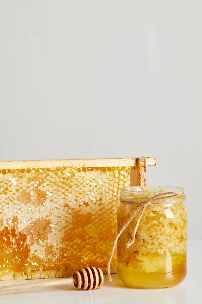 Vista de cerca de la miel de madera más profunda, tarro de vidrio con miel y pila de cera de abejas sobre una mesa blanca sobre fondo gris - foto de stock