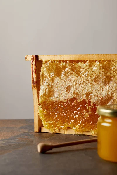 Vista cercana del frasco de vidrio con miel, cera de abeja y miel de madera más profunda sobre fondo gris - foto de stock