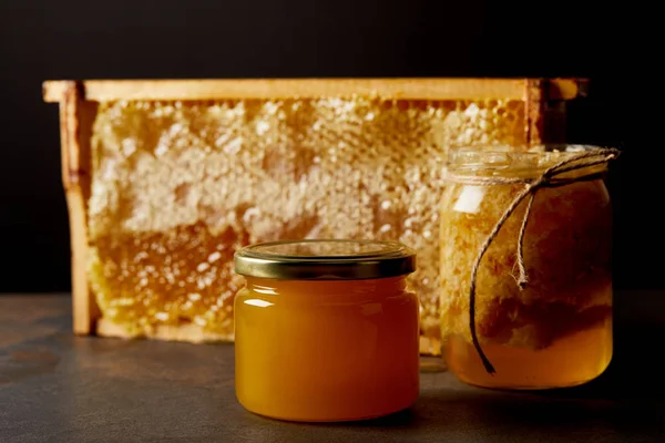 Close up view of glass jars with honey and beeswax on grungy tabletop on black backdrop — Stock Photo