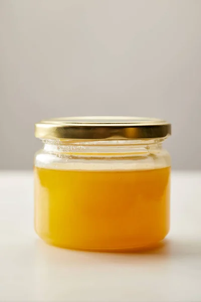 Close up view of sweet organic honey in glass jar on grey backdrop — Stock Photo