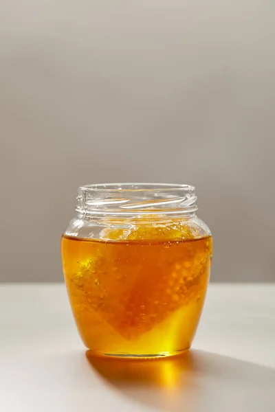 Close up view of opened glass jar with honey and beeswax on grey background — Stock Photo