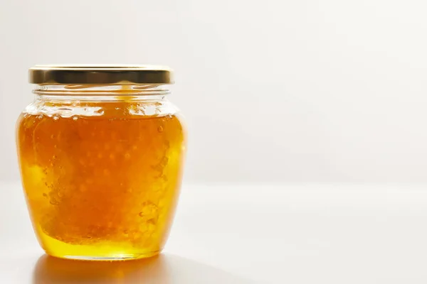 Close up view of honey and beeswax in glass jar on white background — Stock Photo
