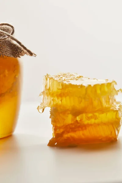 Vista de perto da pilha de cera de abelha e frasco de vidro com mel na mesa branca — Fotografia de Stock