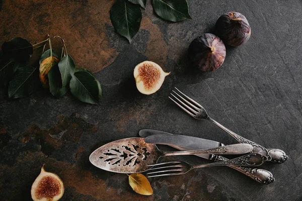 Top view of antique cutlery, green leaves and figs on grungy surface — Stock Photo