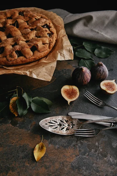 Close up view of homemade pie on baking paper, antique cutlery and fresh figs on dark tabletop — Stock Photo
