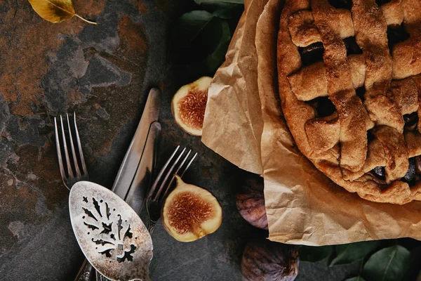 Top view of homemade pie on baking paper, antique cutlery and fresh figs on dark tabletop — Stock Photo