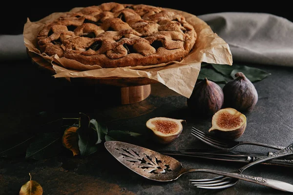 Nahaufnahme von hausgemachtem Kuchen auf Backpapier, antikem Besteck und frischen Feigen auf dunkler Tischplatte — Stockfoto