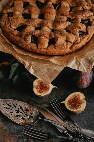 Close up view of homemade pie on baking paper, antique cutlery and fresh figs on dark tabletop — Stock Photo