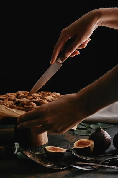 Tiro recortado de mujer cortando pastel en papel de hornear con cuchillo en la superficie con higos - foto de stock