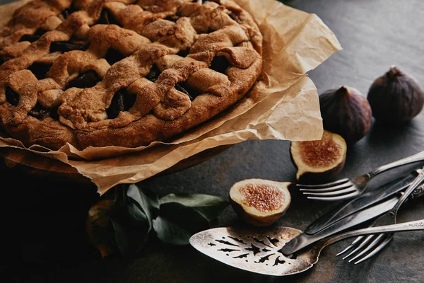 Nahaufnahme von hausgemachtem Kuchen auf Backpapier, antikem Besteck und frischen Feigen auf dunkler Tischplatte — Stockfoto