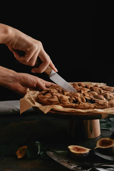 Plan recadré de femme coupant tarte sur papier cuisson avec couteau sur table avec des figues — Photo de stock