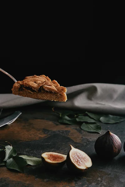 Nahaufnahme eines Kuchenstücks auf dem Tortenserver und Feigen auf dunkel grunziger Oberfläche mit schwarzem Hintergrund — Stockfoto