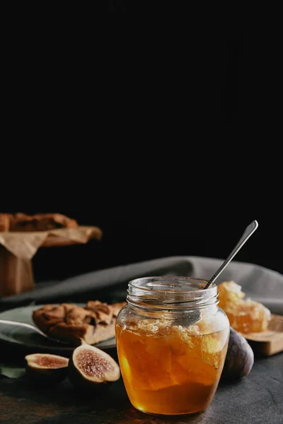 Close up view of glass jar with honey, figs and baked pie on dark surface — Stock Photo