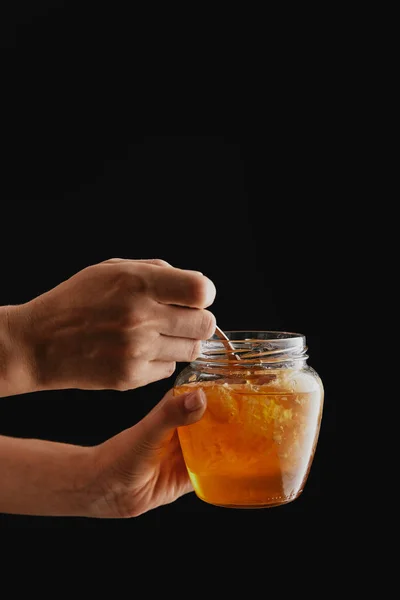 Teilansicht einer Frau mit Glas mit natürlichem Honig isoliert auf schwarz — Stockfoto