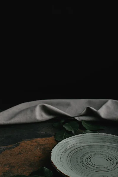 Close up view of empty plate, green leaves and linen on grungy tabletop — Stock Photo