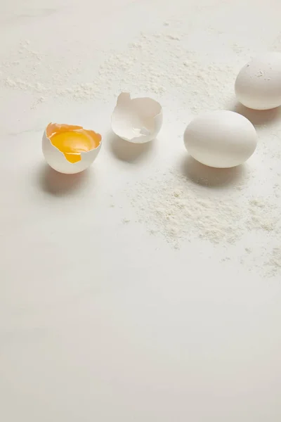 Vista de perto de ovos de galinha crus e farinha em mesa de mármore branco — Fotografia de Stock