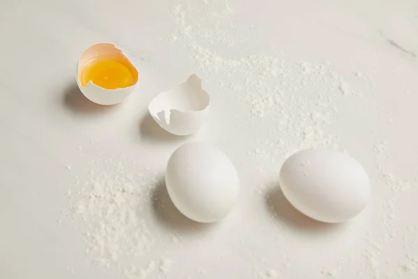 Close up view of raw chicken eggs and flour on white marble tabletop — Stock Photo