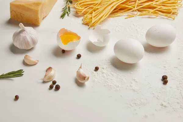 Vista de cerca de macarrones sin cocer e ingredientes para pasta en la superficie blanca - foto de stock