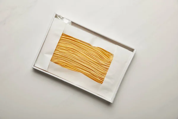 Вид сверху на сырые макароны в белой коробке на мраморной поверхности — стоковое фото