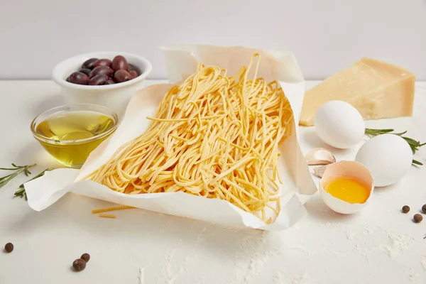 Vue rapprochée de l'arrangement des macaronis non cuits et d'autres ingrédients pour la cuisson des pâtes sur table blanche — Photo de stock