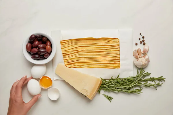 Vue partielle de la femme et des ingrédients de pâtes italiennes sur table en marbre blanc — Photo de stock