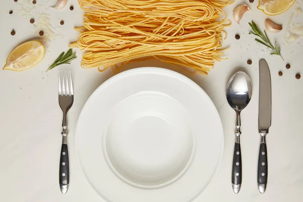 Flat lay with empty plate and pasta ingredients on white marble surface — Stock Photo