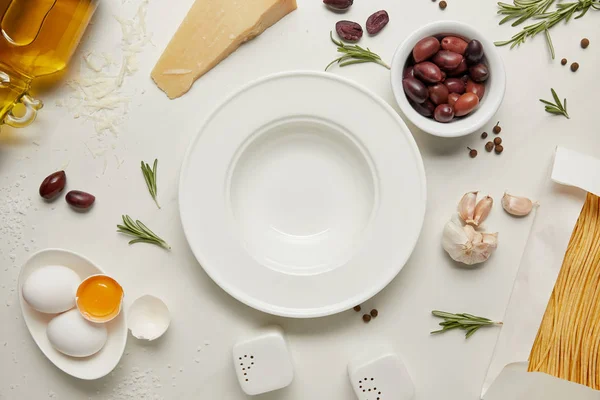 Плоский шар з порожньою тарілкою та інгредієнтами макаронних виробів на поверхні білого мармуру — стокове фото