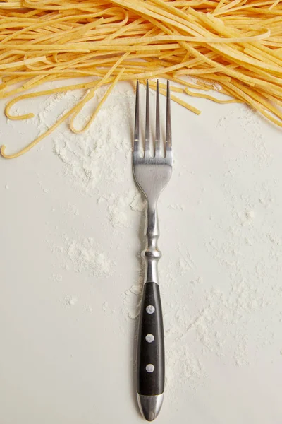 Vista superior de tenedor, macarrones y harina en la superficie blanca - foto de stock