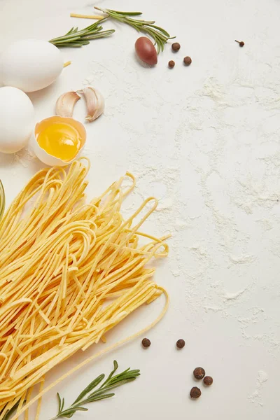 Close up view of uncooked macaroni, raw chicken eggs and flour for cooking pasta arranged on white surface — Stock Photo