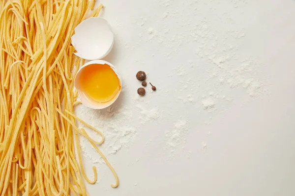 Vista superior de macarrones sin cocer, huevo de pollo crudo y harina para cocinar pasta dispuesta en superficie blanca - foto de stock
