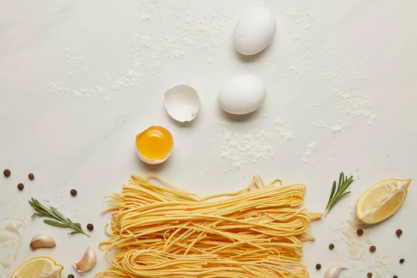 Top view of uncooked macaroni, raw chicken eggs and rosemary for italian pasta arranged on white surface — Stock Photo