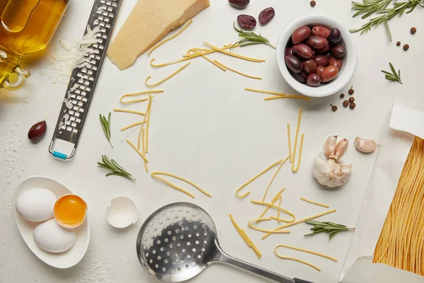 Flache Lage mit italienischen Nudelzutaten, Schöpfkelle und Reibe auf weißer Tischplatte angeordnet — Stockfoto