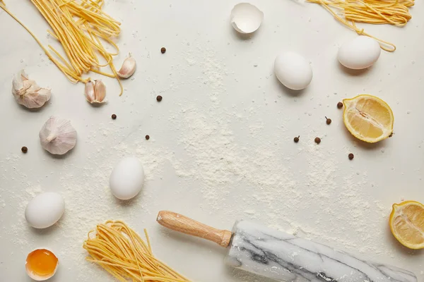 Flat lay com rolo e ingredientes para massas italianas dispostos em mesa de mármore branco — Fotografia de Stock