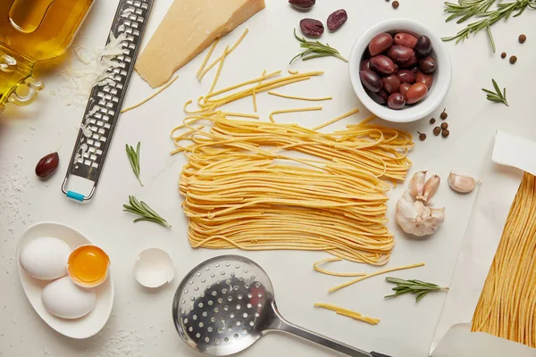 Yacía plano con ingredientes de pasta italiana, cucharón y rallador dispuestos en la mesa blanca - foto de stock