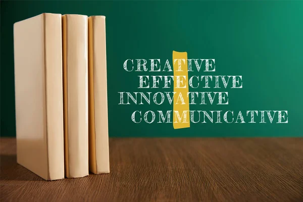 Drei Bücher auf Holztisch mit Kreidetafel auf Hintergrund mit kreativen, effektiven, innovativen, kommunikativen Worten — Stockfoto