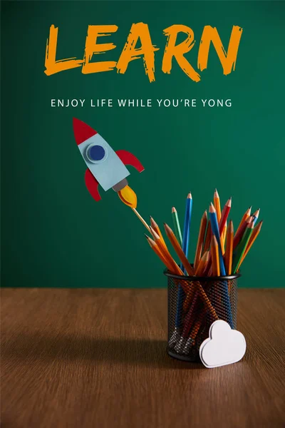 Colorful pencils, rocket, cloud sign on wooden table with chalkboard on background with 