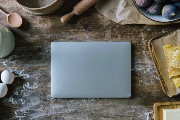 Vista dall'alto del computer portatile su un tavolo di legno disordinato con farina versata e ingredienti da forno — Foto stock