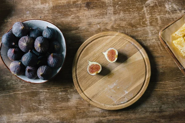 Halves of fig on cutting board and pile in bowl on rustic wooden table — Stock Photo