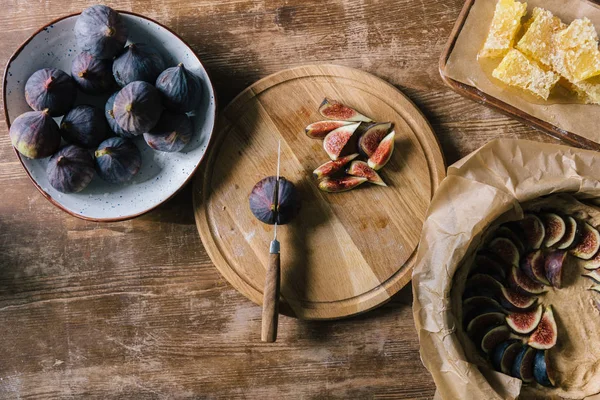 Груда инжира в миске и на разделочной доске на деревенском деревянном столе во время приготовления пирога — стоковое фото