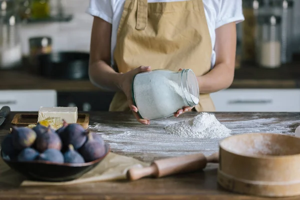 Abgeschnittene Aufnahme einer Frau, die Mehl auf einen rustikalen Holztisch mit Zutaten für Feigenkuchen gießt — Stockfoto