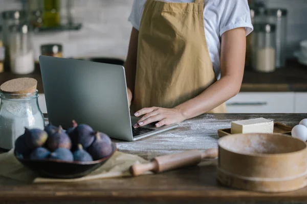 Cropped shot of woman using laptop during pie preparation — Stock Photo