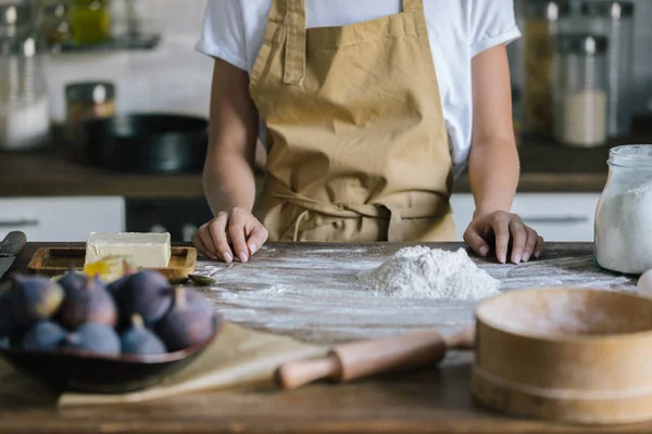 Schnappschuss einer Frau in Schürze, die vor rustikalem Holztisch mit Kuchenzutaten steht — Stockfoto