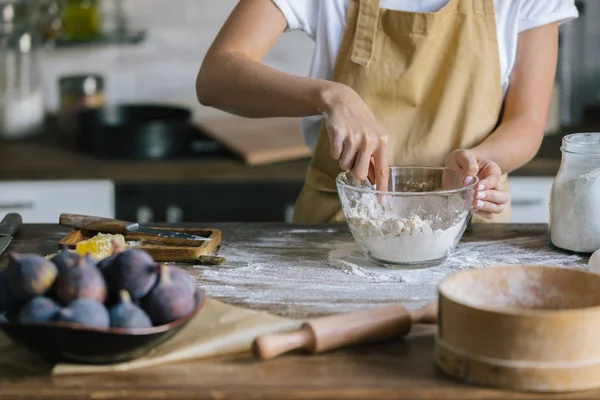 Tiro recortado de mujer en delantal mezcla de masa para pastel con cuchara en mesa de madera rústica - foto de stock