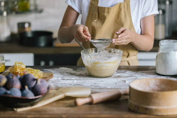 Tiro recortado de la mujer derramando harina en un tazón con tamiz durante la preparación del pastel - foto de stock