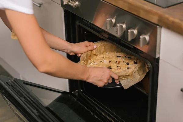 Recortado tiro de mujer poniendo pastel en horno - foto de stock