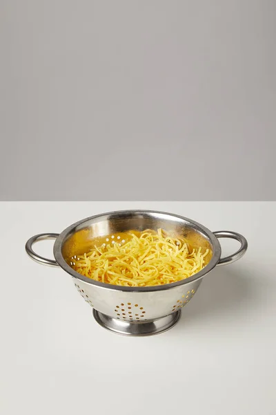 Passoire en métal avec spaghettis cuits sur table blanche — Photo de stock