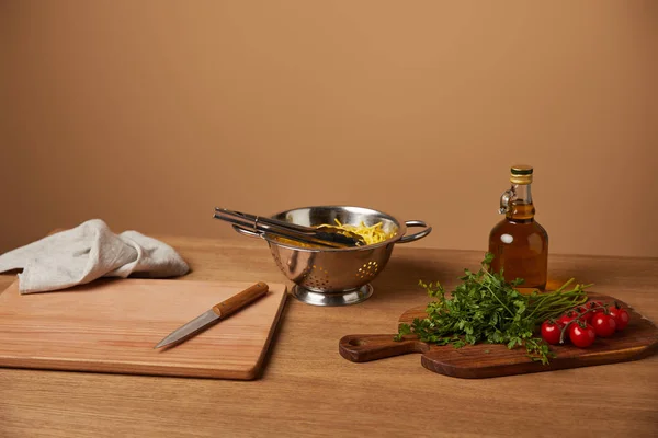Спагетти в металлическом дуршлаге с овощами и оливковым маслом на деревянном столе — стоковое фото